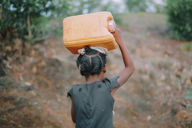 child carries large water bottle on head